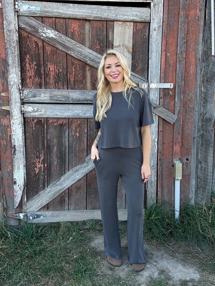 Woman in a grey lounge outfit standing in front of a rustic wooden door.