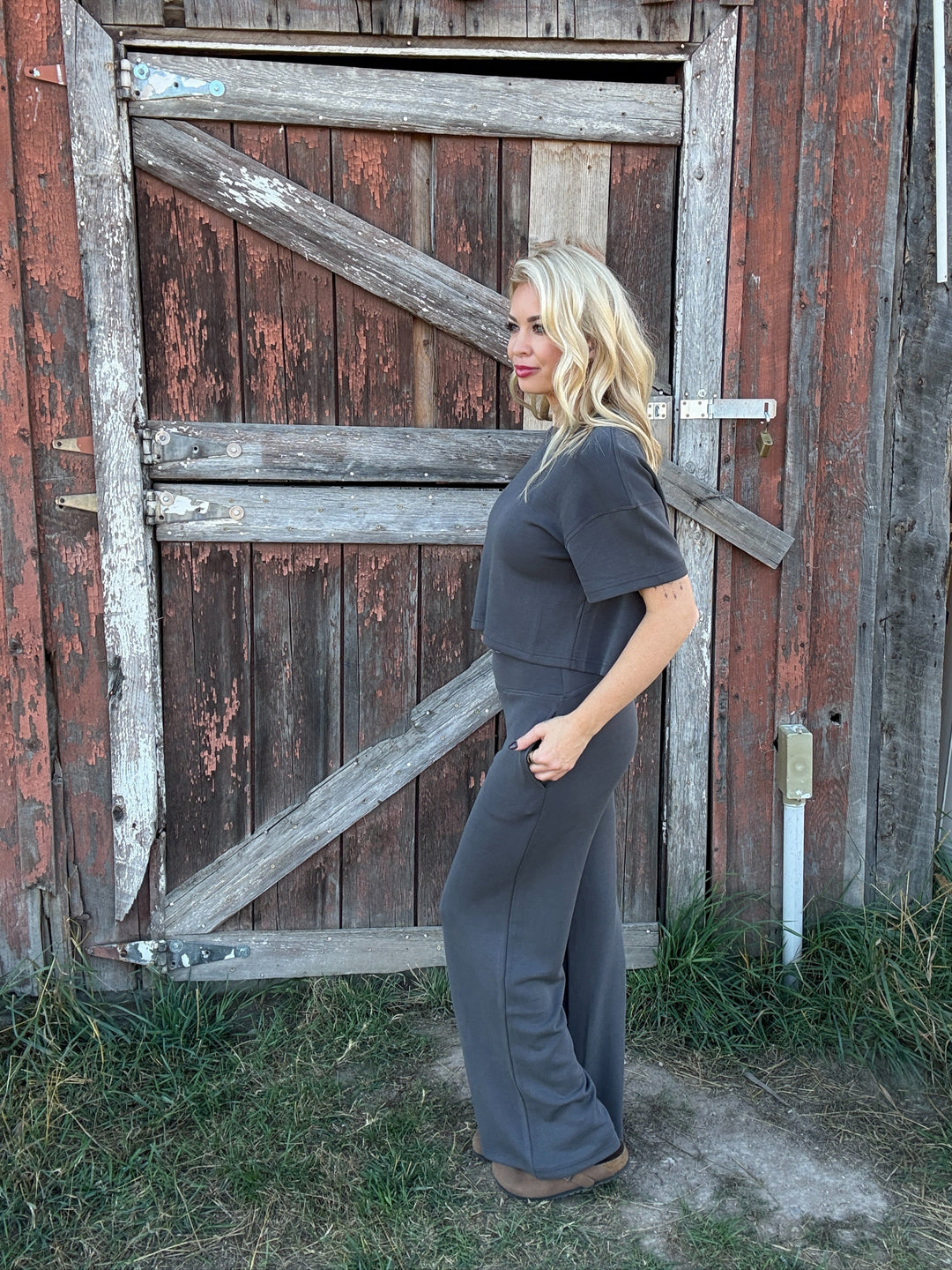 Woman in a gray lounge outfit standing in front of a rustic wooden barn door.