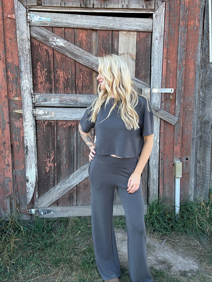 Woman in a grey lounge set standing in front of a rustic wooden door.