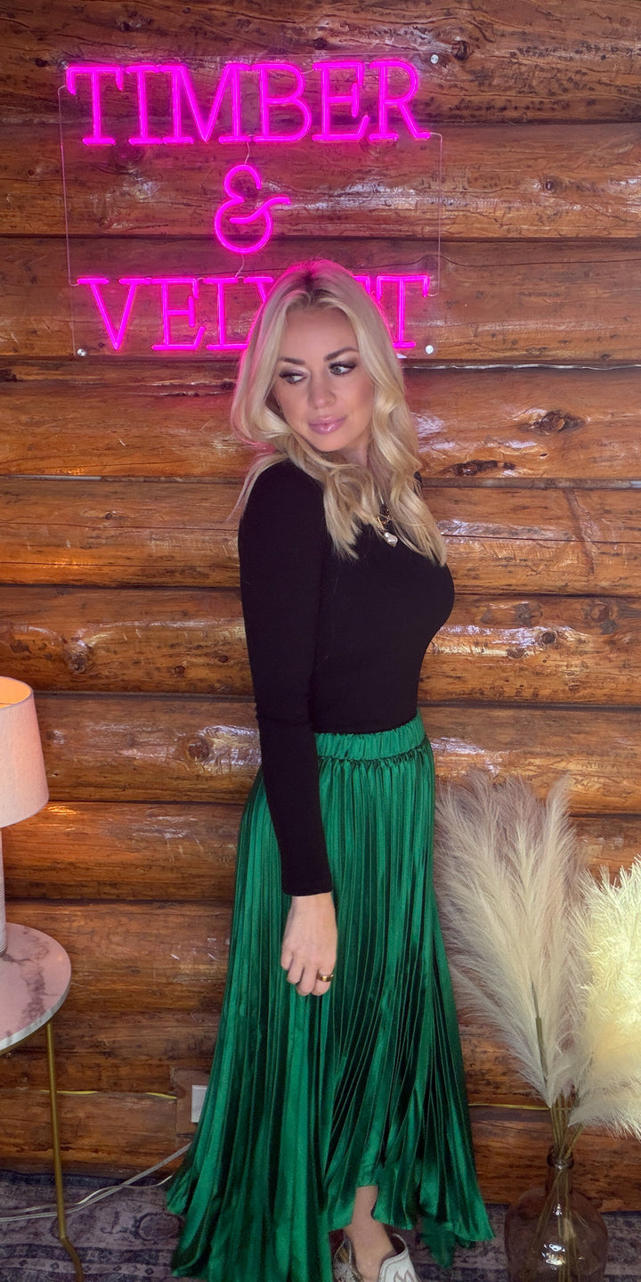 Woman in a green skirt standing in front of a wooden wall with 'TIMBER & VELVET' neon sign.