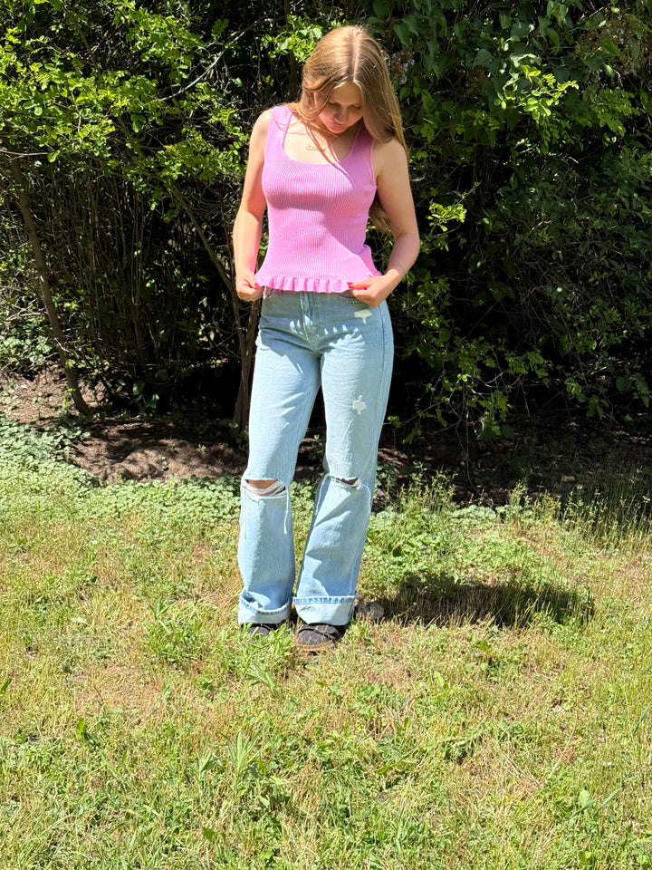 Woman in pink top and blue jeans standing in a grassy area with greenery.