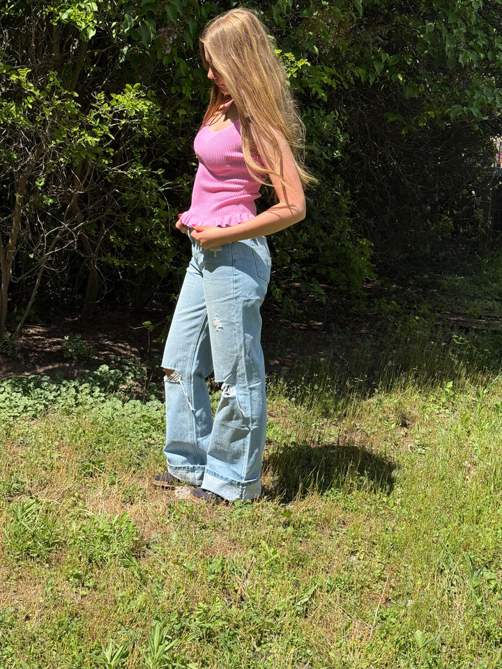 Woman in a pink top and blue jeans standing in a grassy area with trees in the background