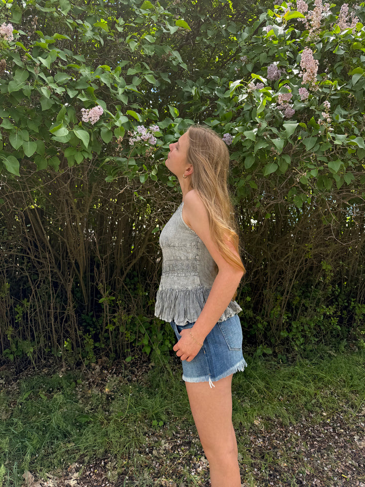Woman wearing a grey tank top standing in a garden with greenery and flowers