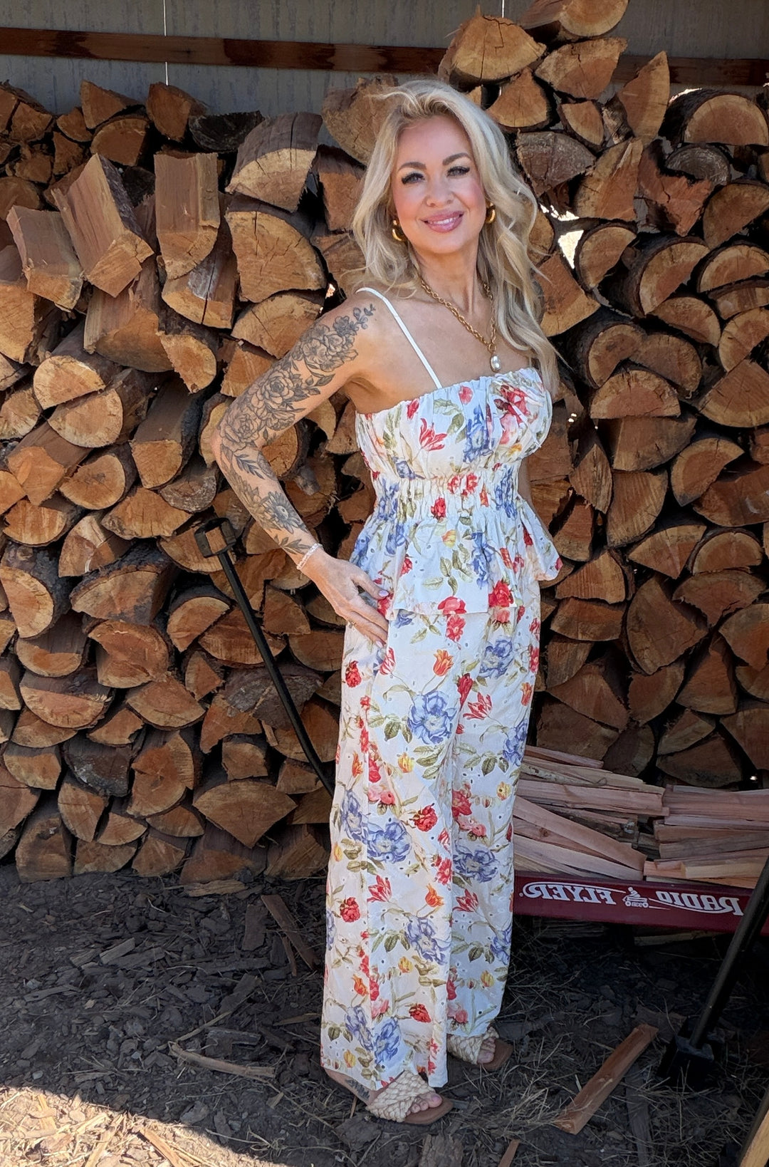 Woman in a floral top & bottoms standing in front of stacked wood