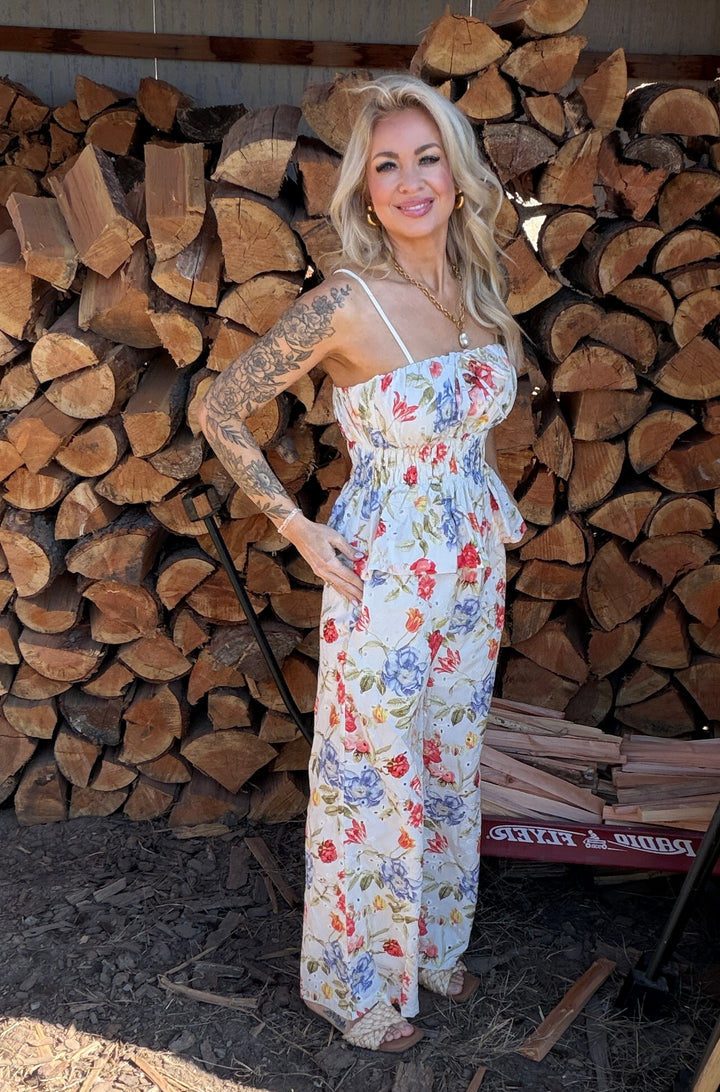 Woman in a floral top & bottoms standing in front of stacked wood