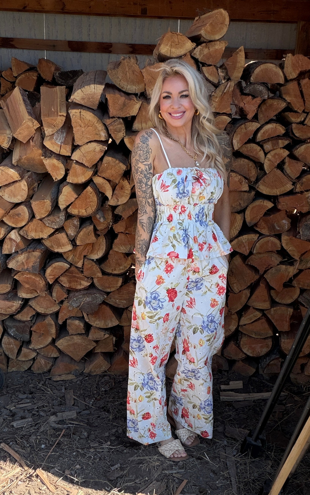 Woman in a floral pants & top standing in front of stacked wood