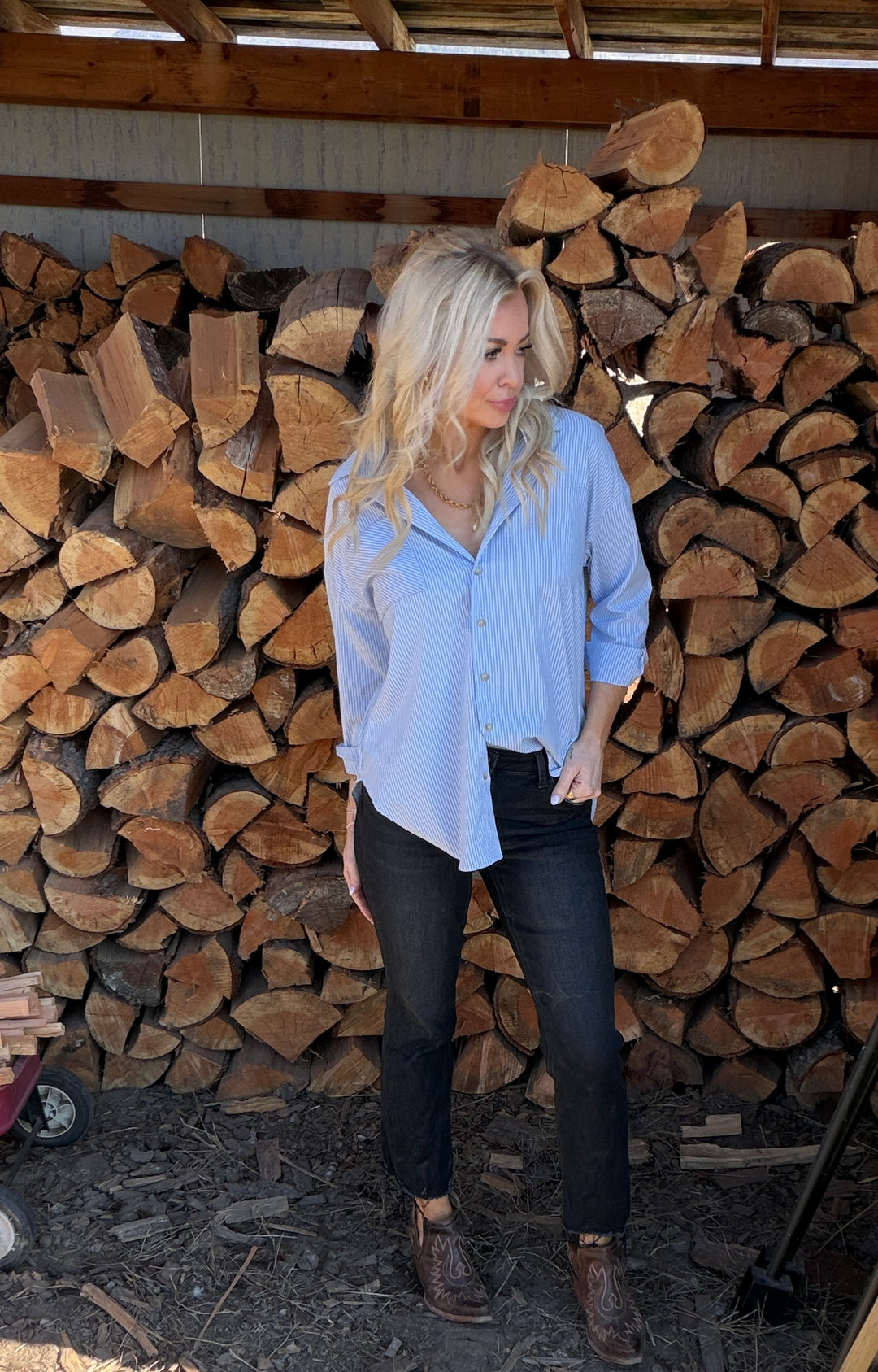 Woman wearing striped top and jeans standing in front of a stack of wood logs