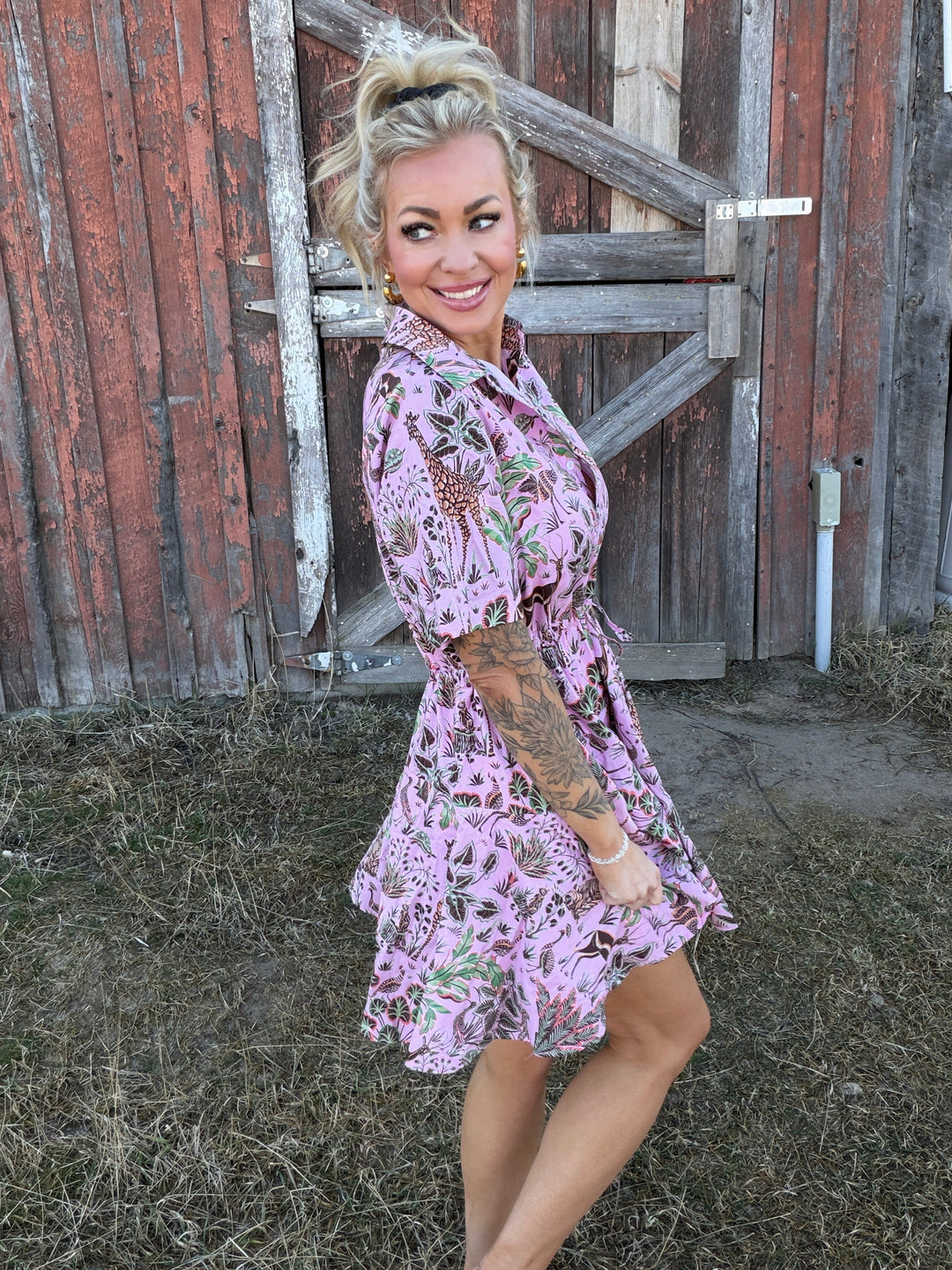Woman in a pink floral dress standing in front of a wooden building.