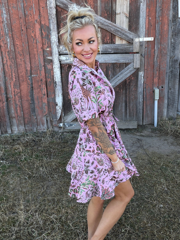 Woman in a pink floral dress standing in front of a wooden building.