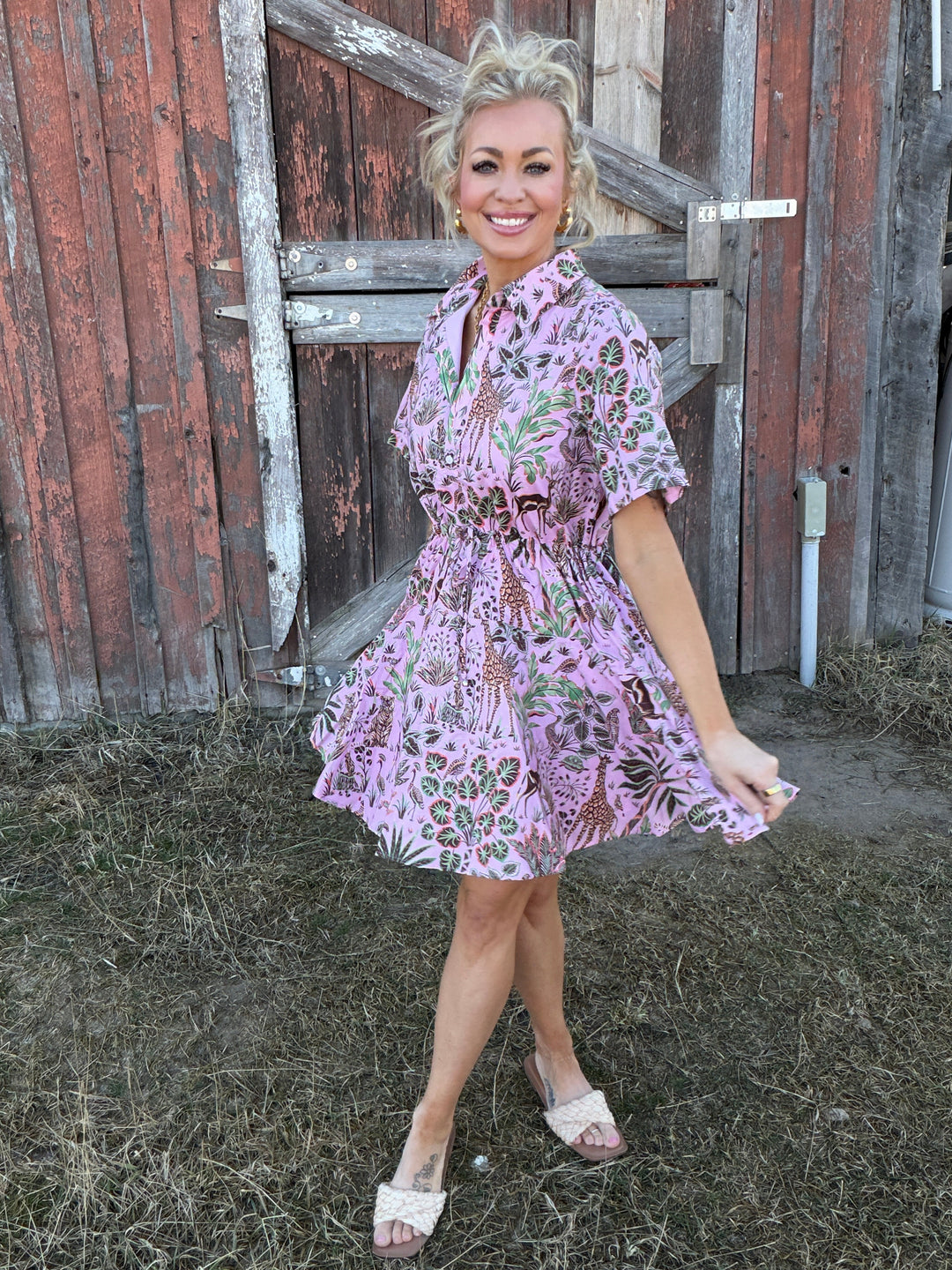 Woman in a pink floral dress standing on a wooden platform with a rustic background