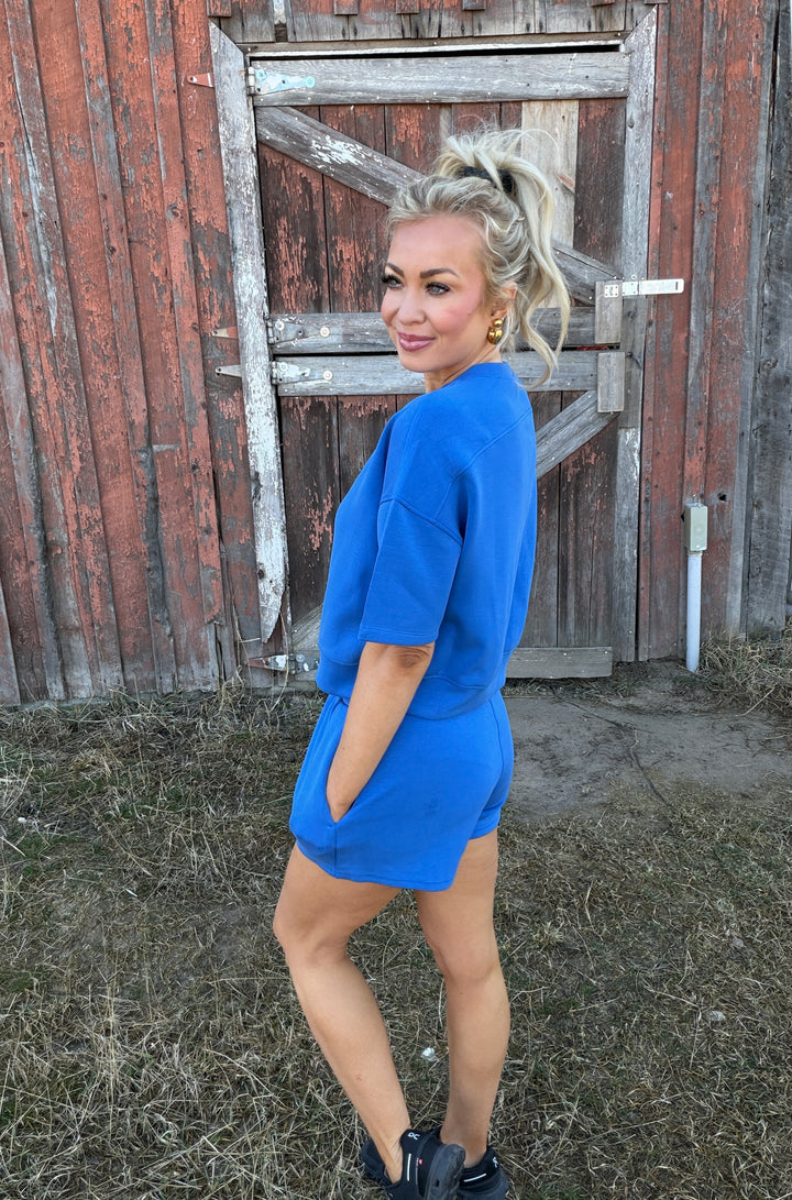 Woman in a blue lounge set outfit standing in front of a rustic wooden door.
