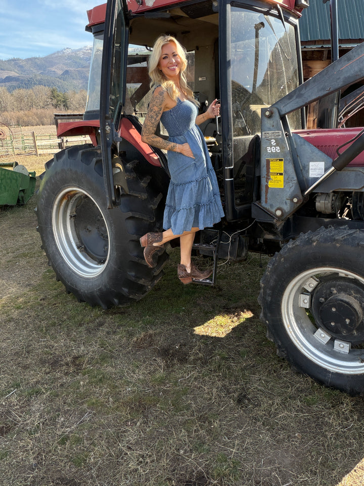 Woman in blue denim dress posing on a tractor 