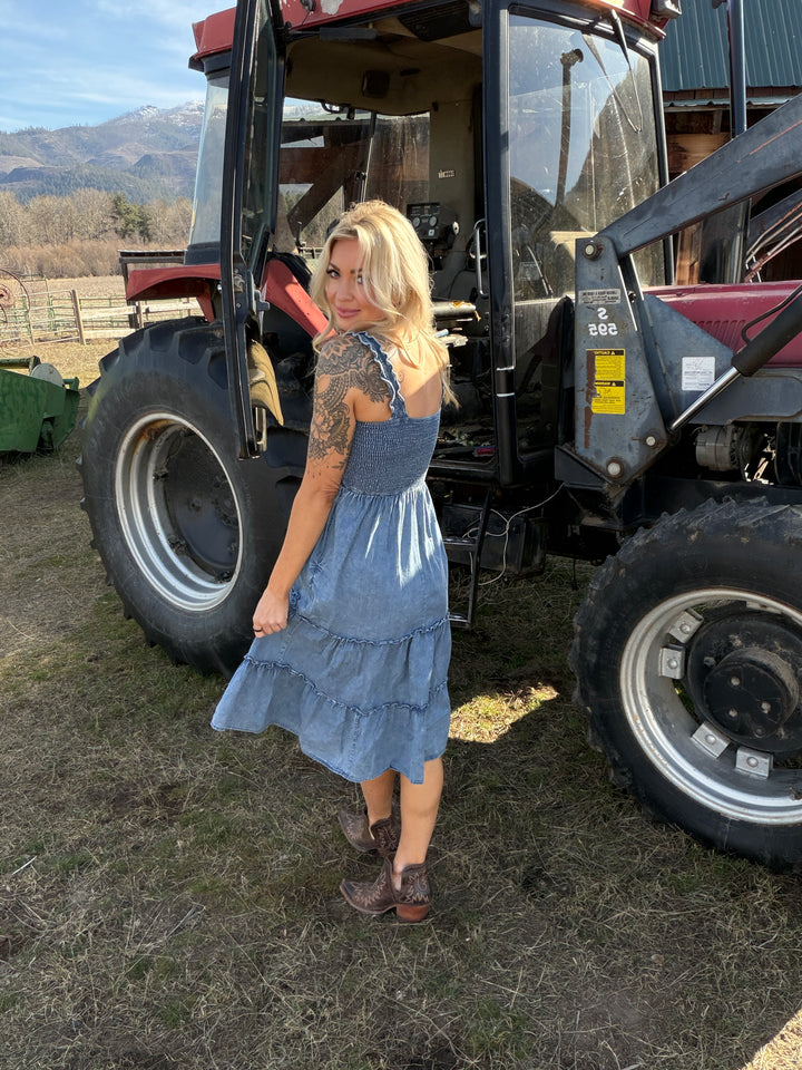 Woman in a blue denim dress standing next to a tractor 