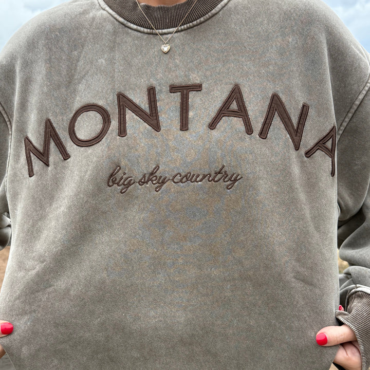Gray sweatshirt with 'Montana' and 'big sky country' text held by a person.