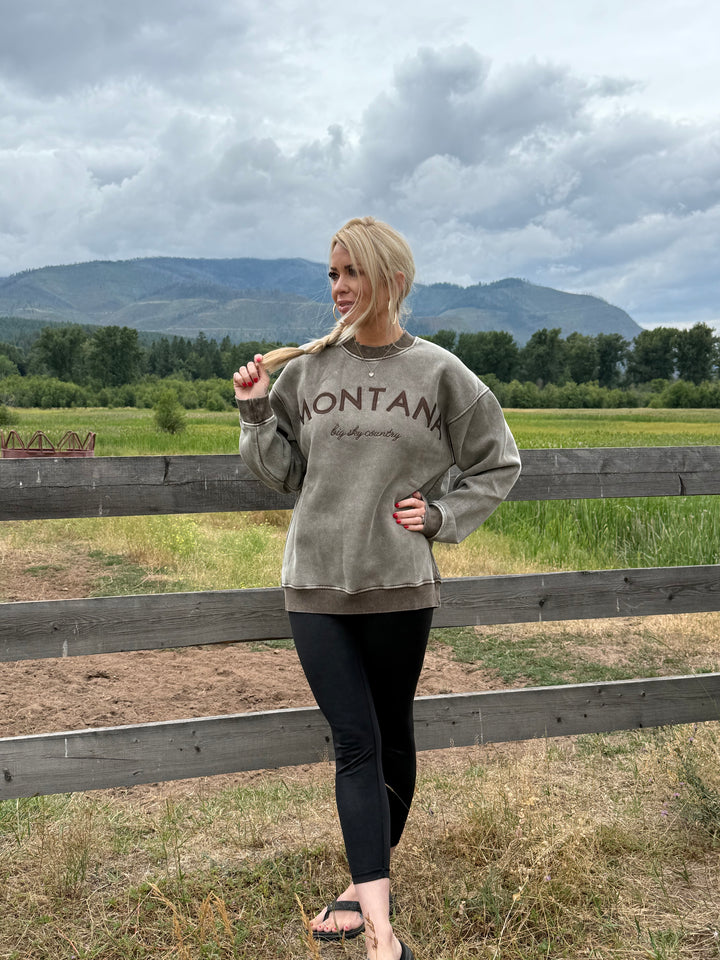 Person wearing a sweatshirt with Montana Big Sky Country Crewneck sweatshirt in acid wash brown