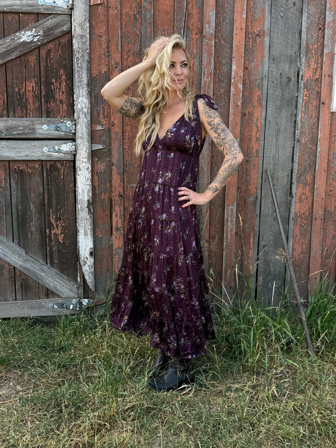 Woman in a purple flower dress with adjustable shoulder ties standing in front of an old barn
