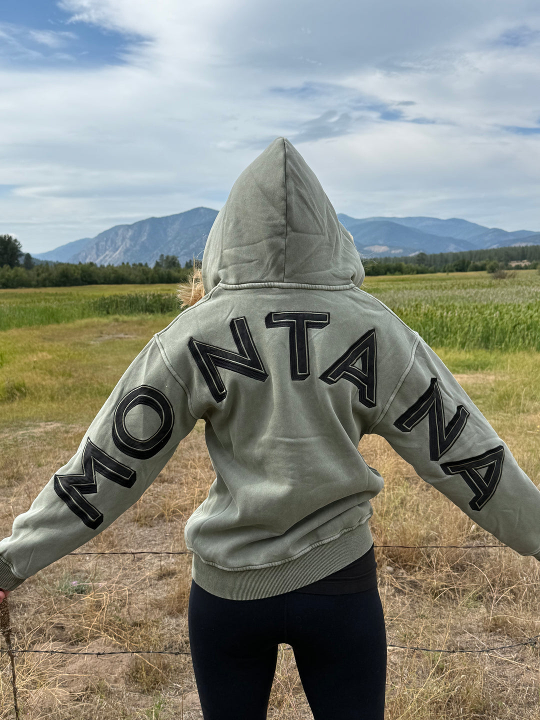 Person wearing a hoodie with 'Montana' text, standing outdoors with a scenic background.