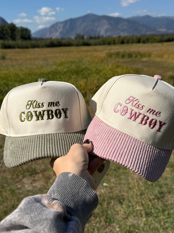 Two cowboy trucker hats held up with a scenic background of mountains and open sky.