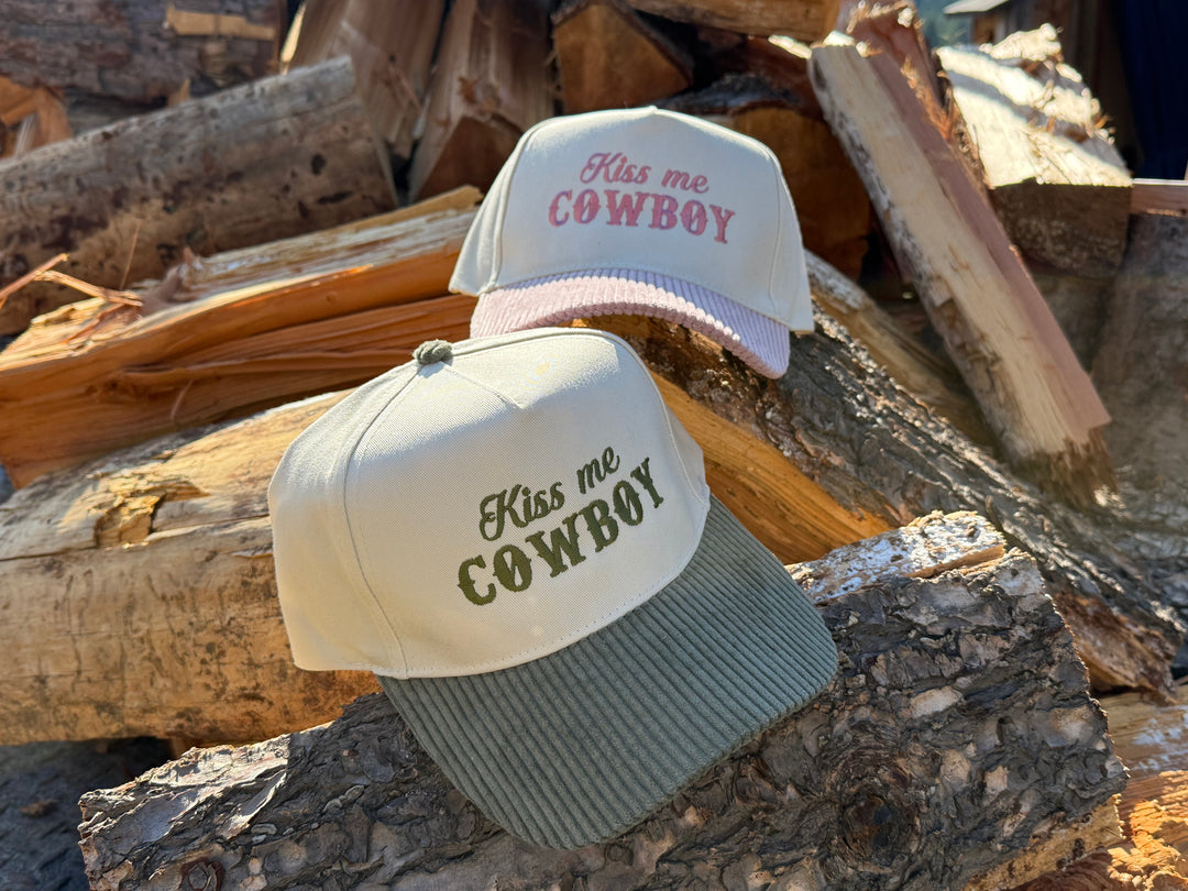 Two 'Kiss me Cowboy' trucker hats on a pile of logs.