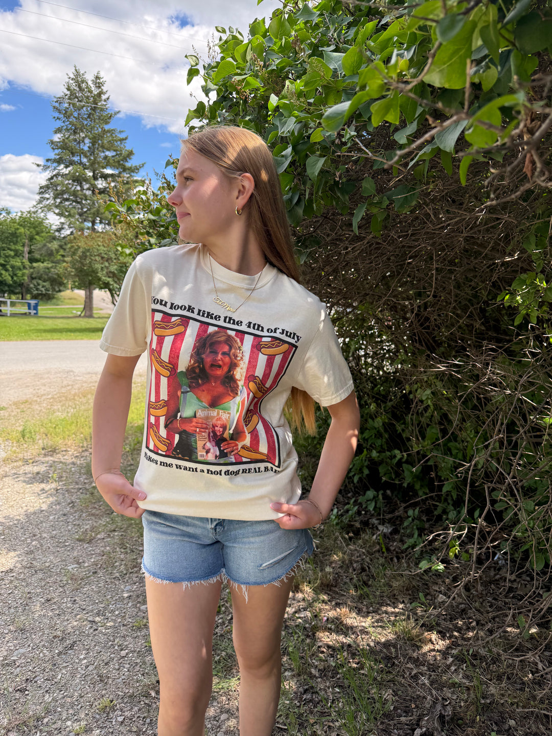 Person wearing a graphic t-shirt 'you look like the 4th of July, makes me want a hot dog real bad' outdoors with trees and sky in the background