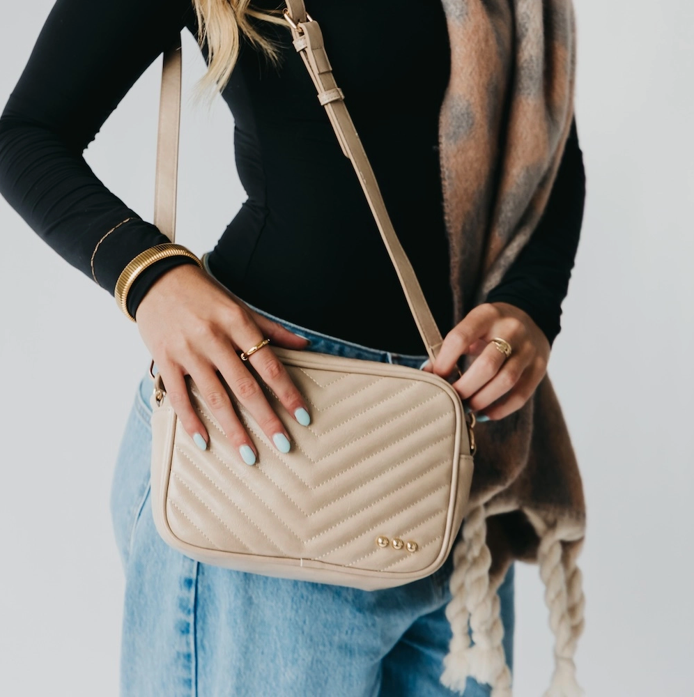 Person holding a beige quilted handbag with a plain background