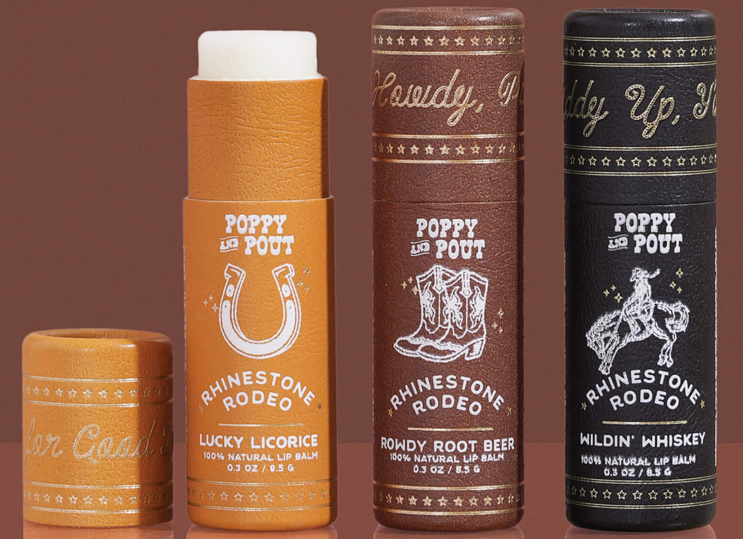 Collection of lip balm Poppy & Pout Rhinestone Rodeo Trio with cowboy-themed labels on a brown background